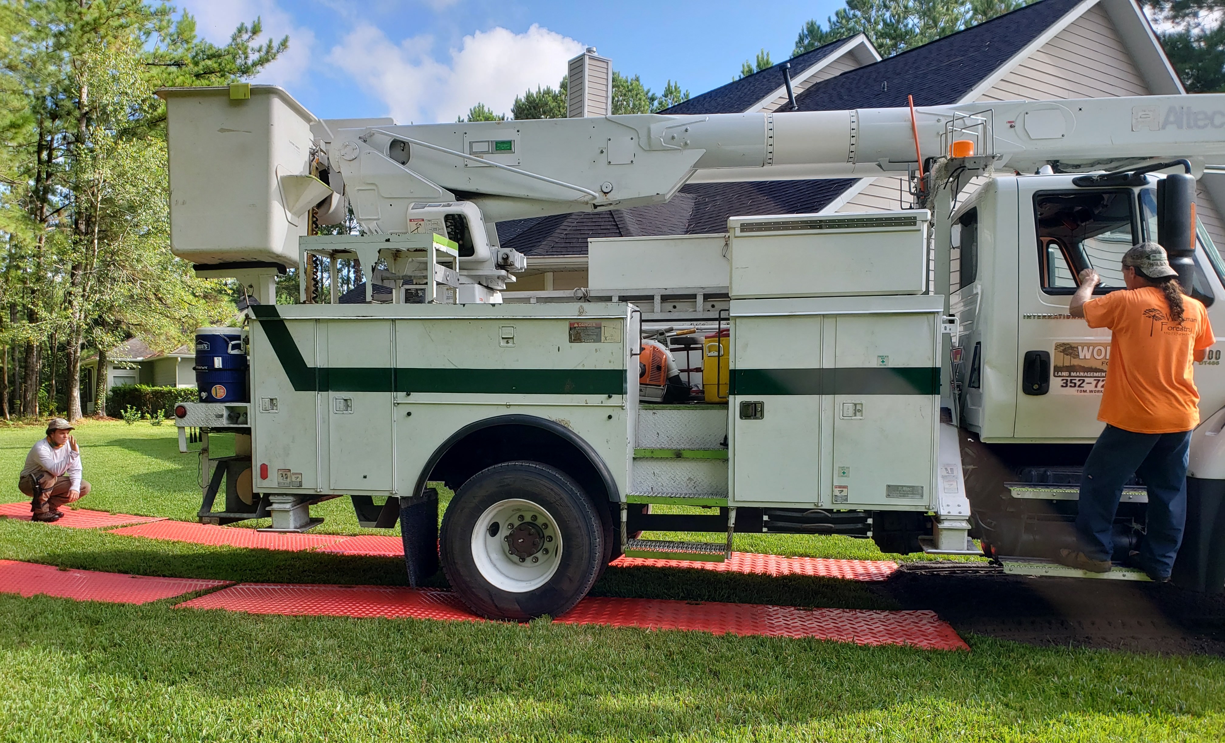 Bucket truck and ground protection mats in use during a tree removal, protecting the lawn from equipment damage